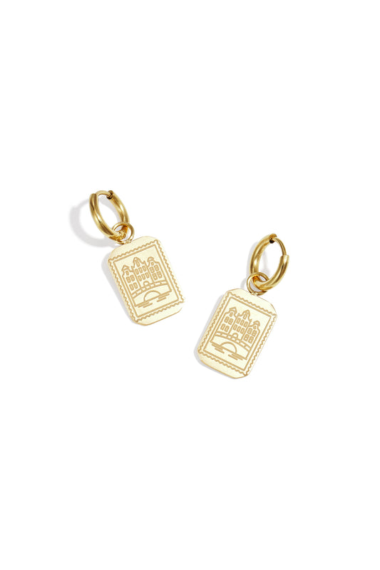 Pair of gold drop earrings featuring rectangular pendants with etched Amsterdam canal house design on a white background.