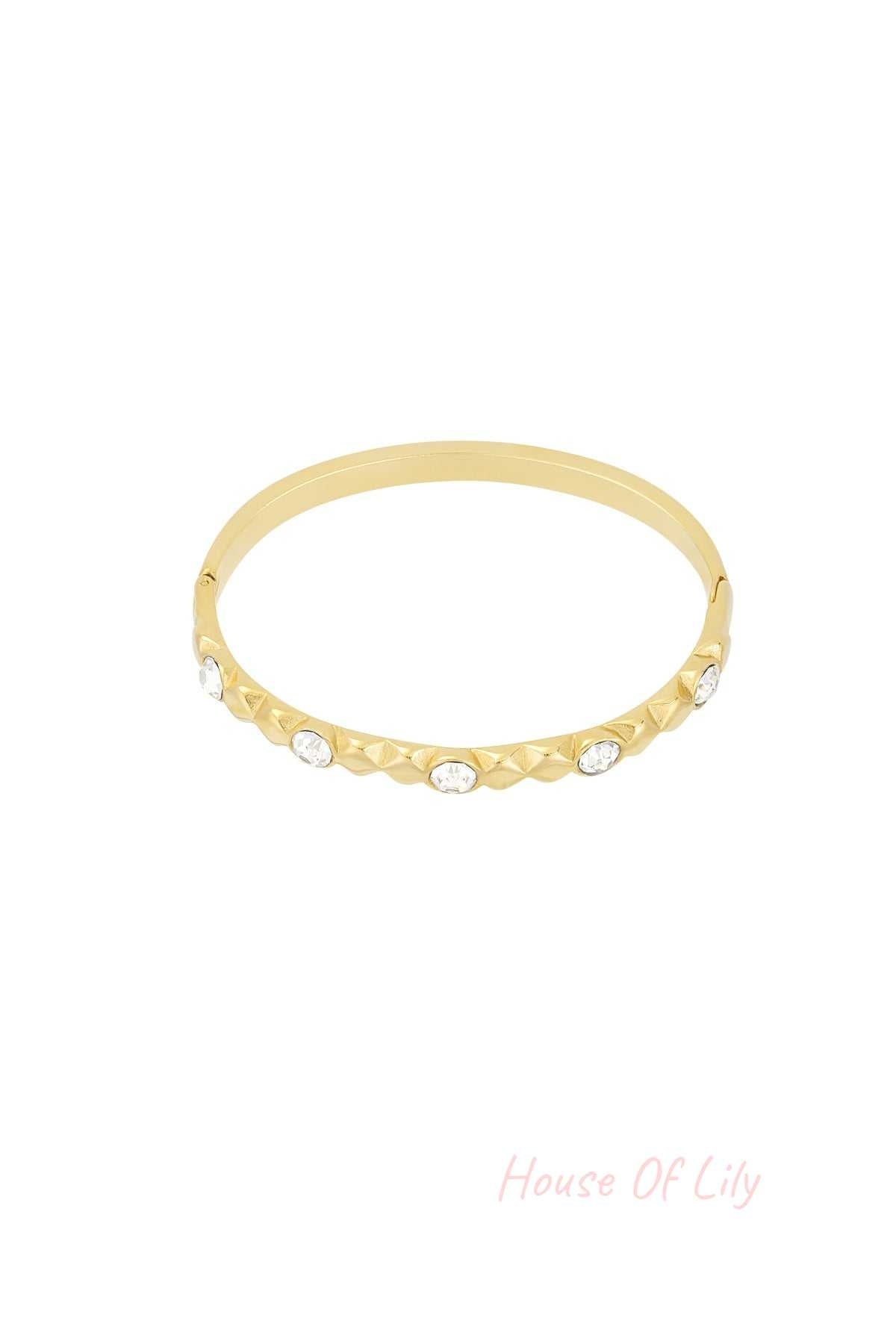 Gold tone crystal studded bangle bracelet with relief design on white background