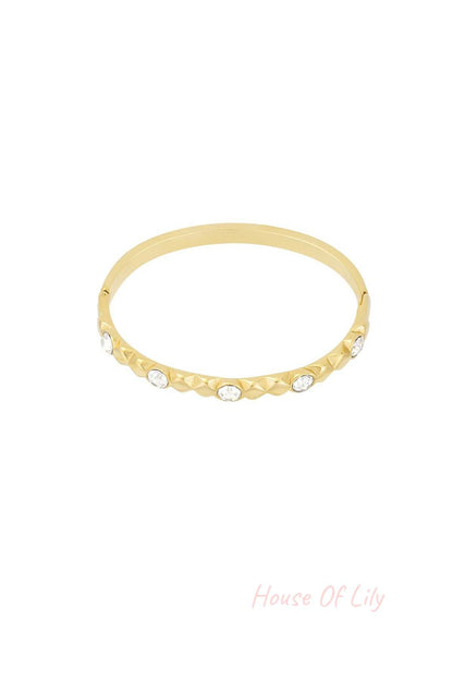 Gold tone crystal studded bangle bracelet with relief design on white background