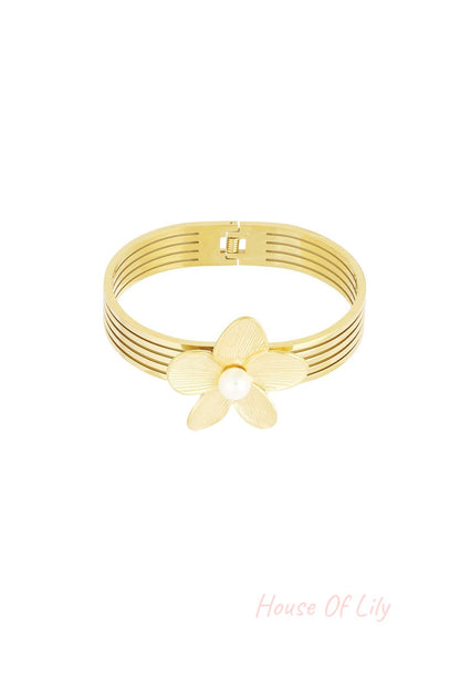 Close-up of a gold-tone multi-strand bangle bracelet featuring a textured flower and central pearl accent on a white background