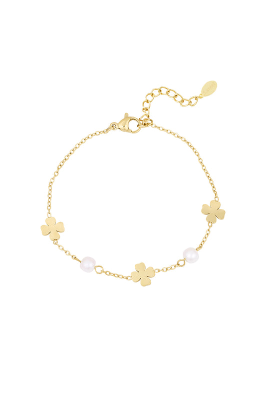 Gold-tone bracelet with clover charms and pearls laid flat on white background