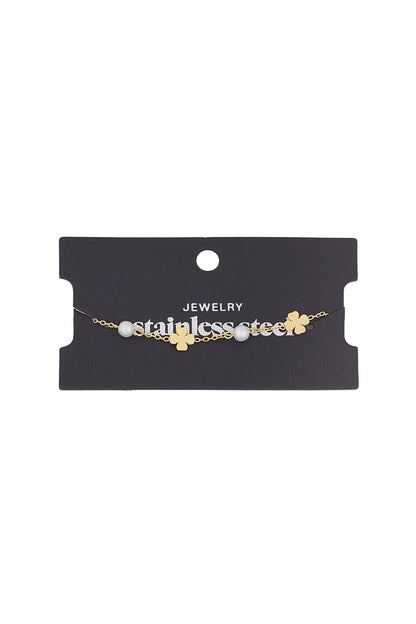 Gold clover and pearl charm bracelet displayed against a black jewellery card labelled stainless steel