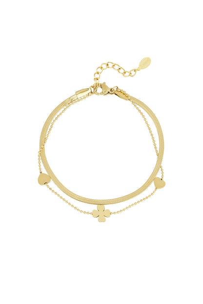 Close-up of a gold layered charm bracelet with small heart and clover charms on a white background