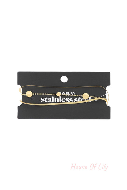 Gold-tone minimal coin charm bracelet displayed on black branded card packaging showing chain and clasp details