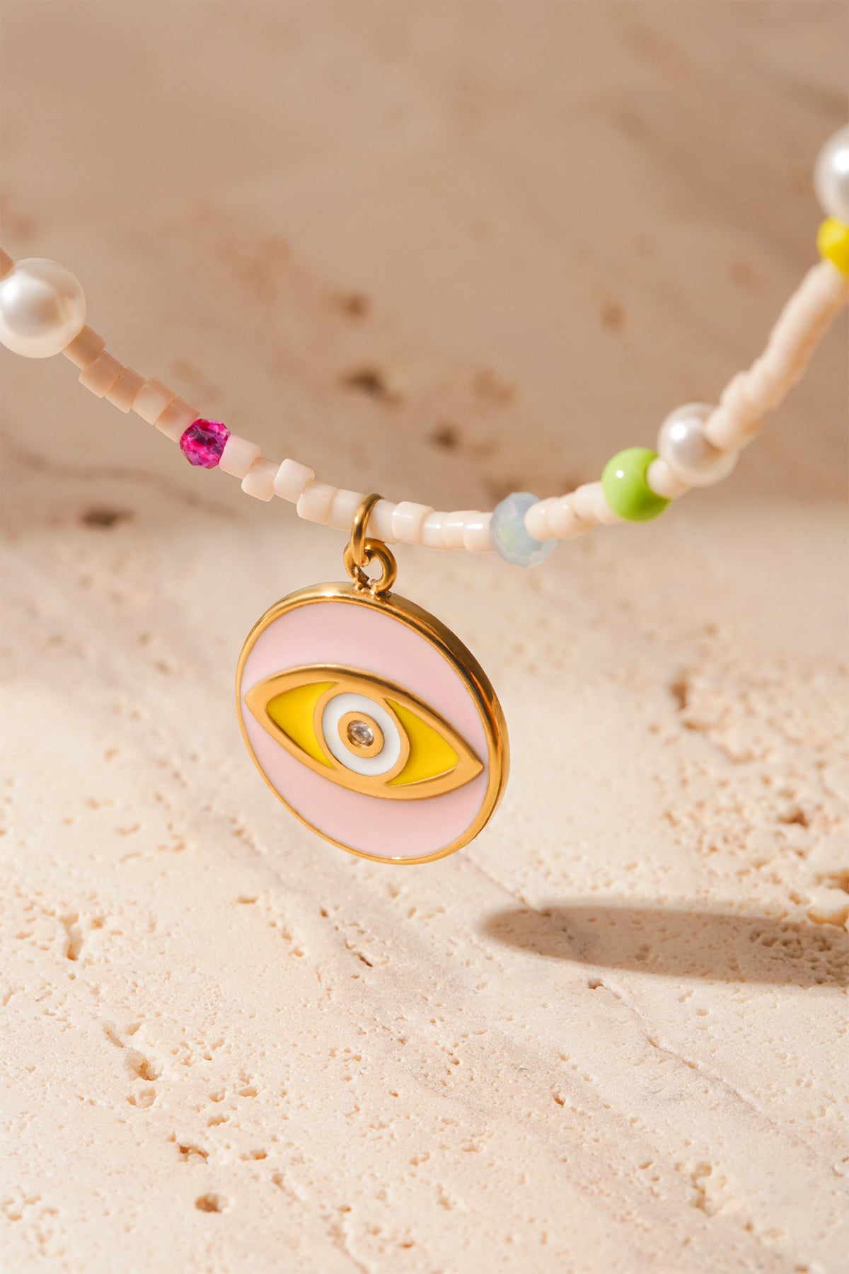Close detailed shot of gold-tone eye charm with pastel pink and yellow enamel on beaded bracelet