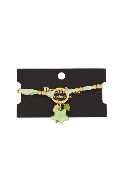 Green fabric charm bracelet displayed on black product card with gold beads and charms