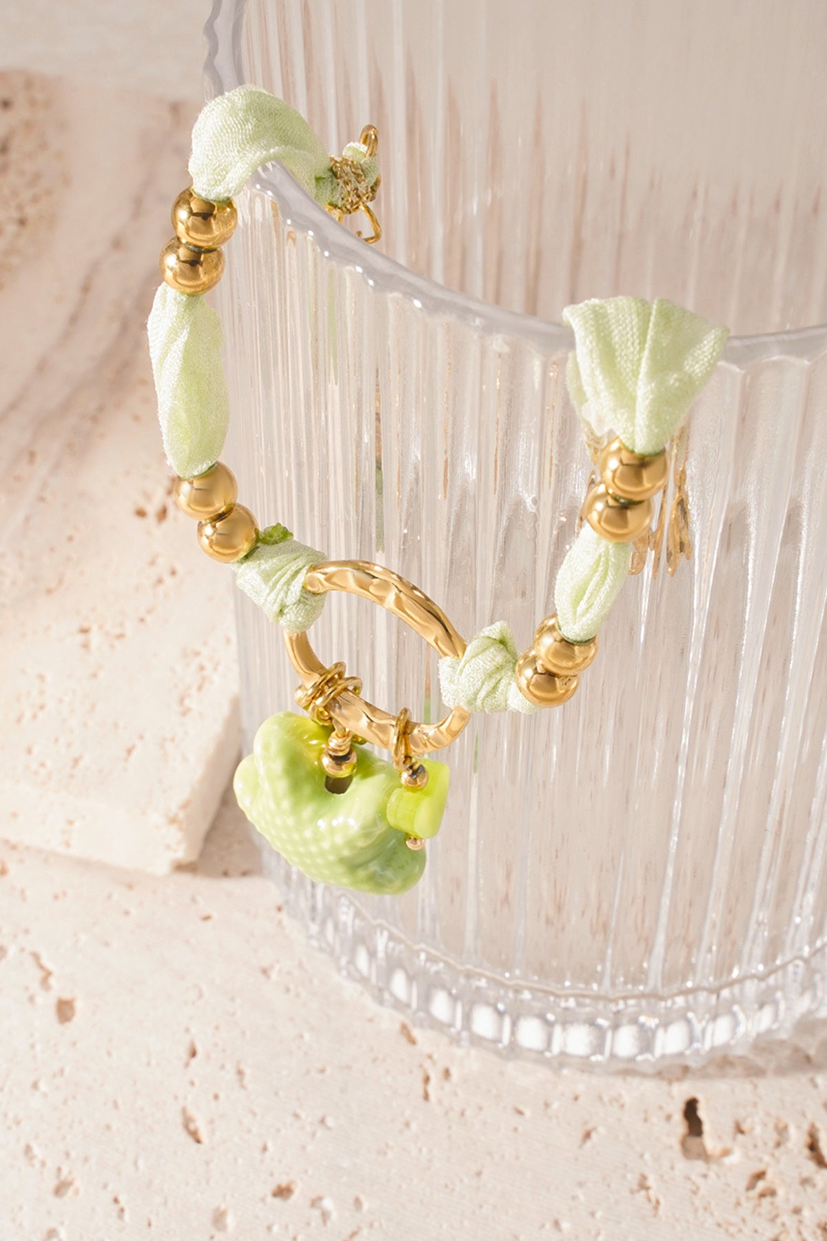 Side view of bracelet draped over glass showing gold beads and green fabric with starfish charm