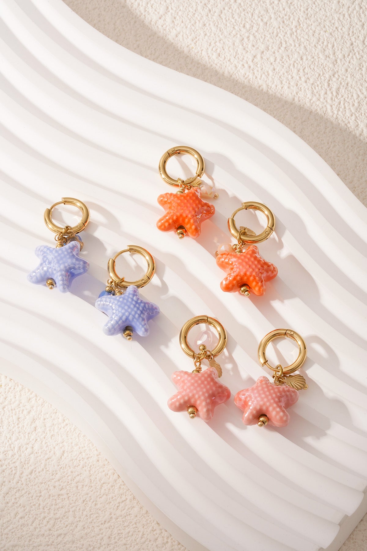 Set of six starfish charm hoop earrings in blue, pink, and orange colors on textured white surface