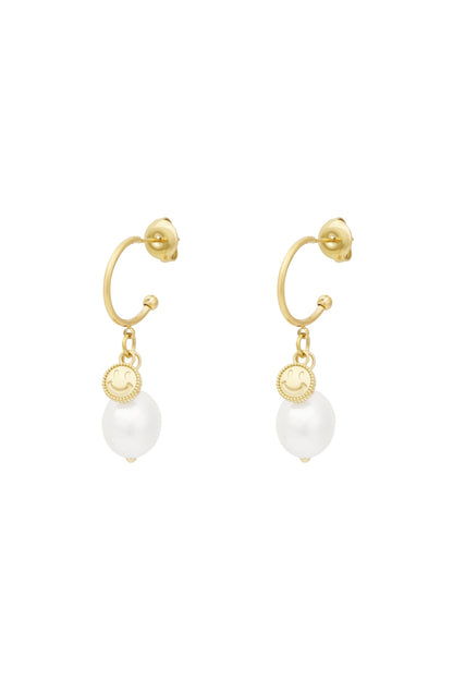 Pair of gold-tone hoop drop earrings featuring a small smiley charm and a white pearl drop against a white background
