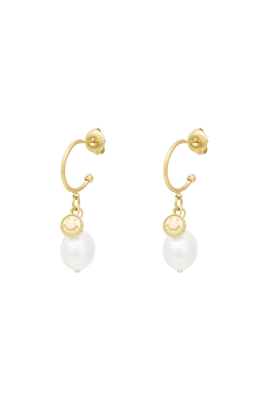 Pair of gold-tone hoop drop earrings featuring a small smiley charm and a white pearl drop against a white background