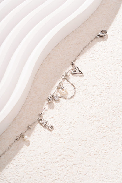 Close up of silver-tone charm bracelet featuring heart, LOVE letter crystals, and faux pearl accents on a light textured background