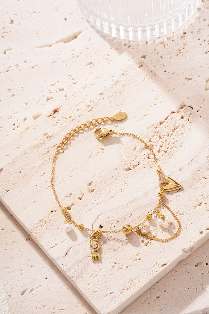 Close shot of gold-tone charm bracelet on textured beige fabric next to a glass