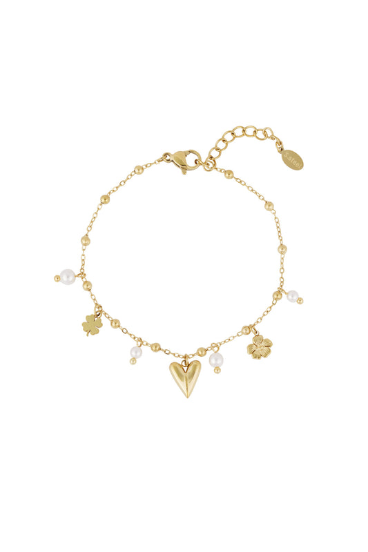 Close-up of delicate gold charm bracelet with heart, flower, four-leaf clover pendants and small pearls on a minimal chain