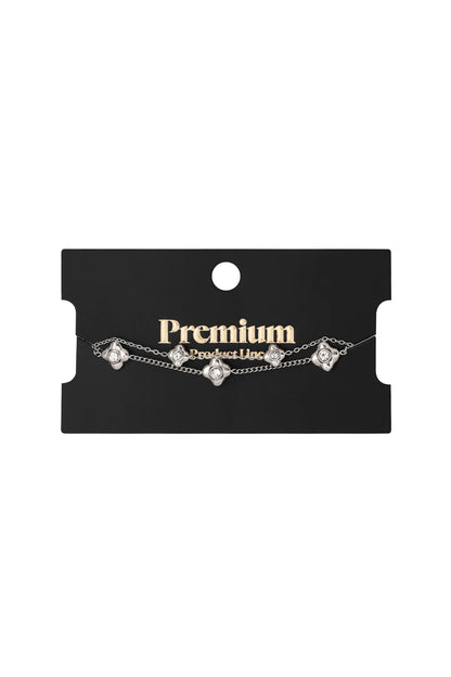 Silver double chain flower charm bracelet displayed on black Premium Product Line card
