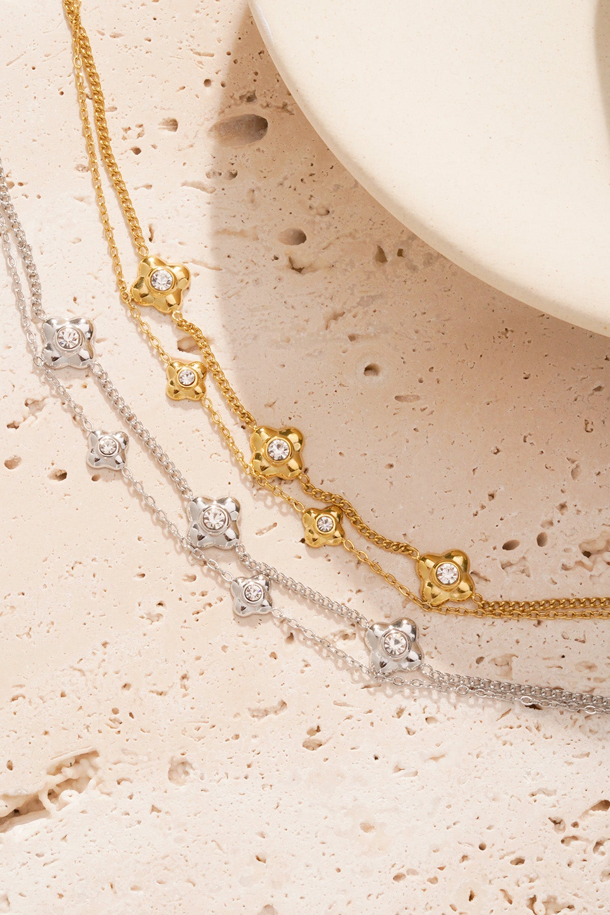 Gold and silver double chain flower charm bracelets placed on textured beige surface
