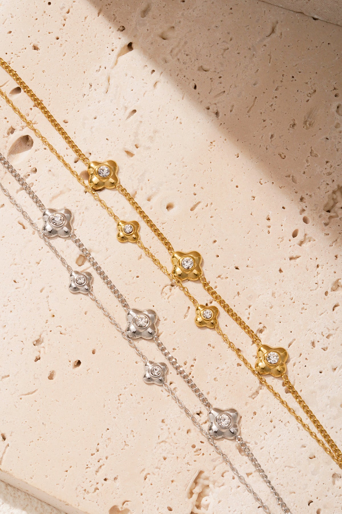 Detailed view of gold and silver flower charm bracelets arranged on light natural stone background
