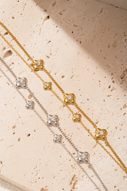 Detailed view of gold and silver flower charm bracelets arranged on light natural stone background