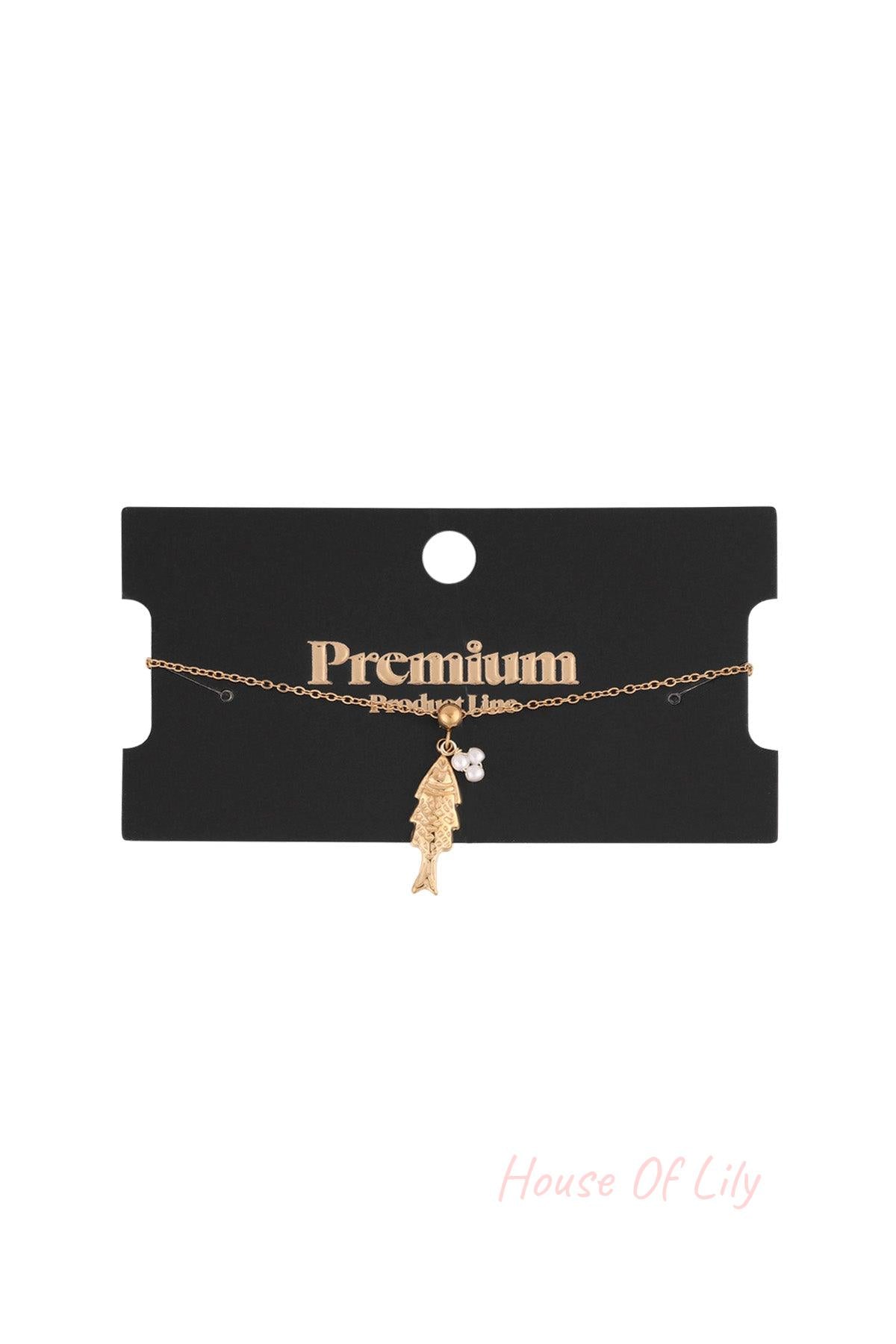 Gold tone fish pendant charm bracelet displayed on a black premium product line card