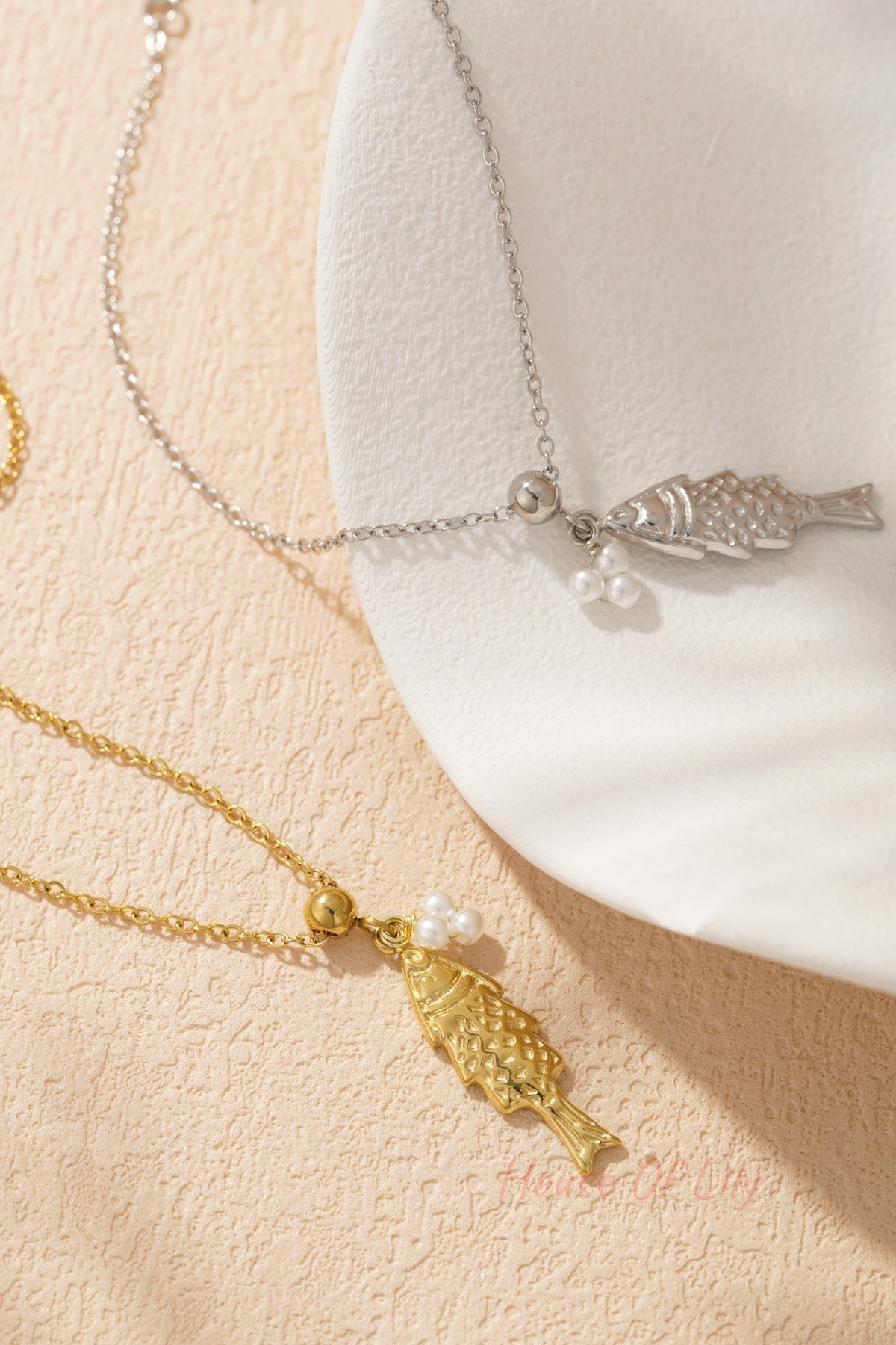 Close-up of silver and gold tone fish pendant charm bracelets paired elegantly on a white textured dish