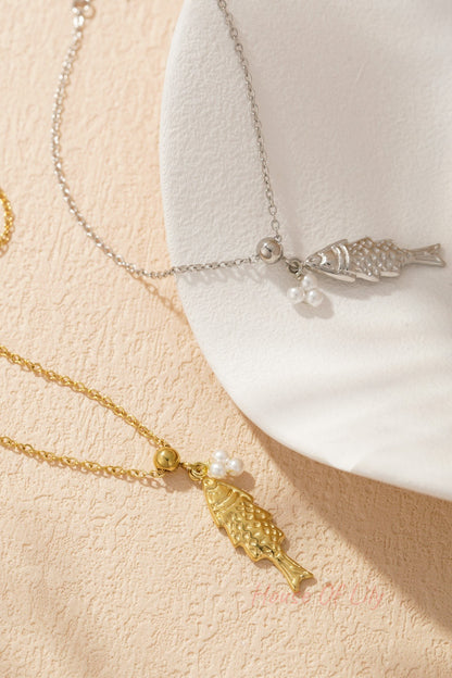 Close-up of silver and gold tone fish pendant charm bracelets paired elegantly on a white textured dish