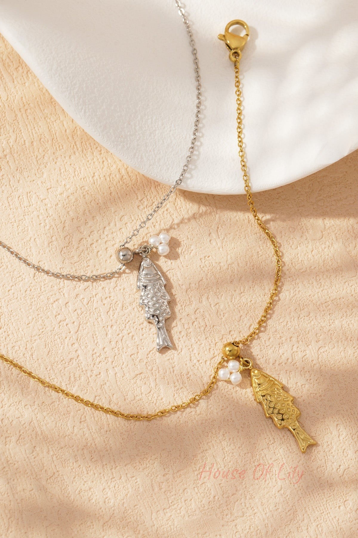 Silver and gold toned charm bracelets with fish pendants and pearl details arranged on a textured background