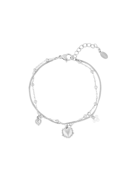 Close-up of silver double charm bracelet featuring heart pendants and pearl clusters on white background