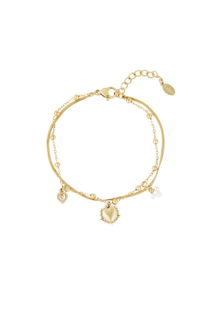 Close-up of gold double charm bracelet featuring heart pendants and pearl clusters on white background