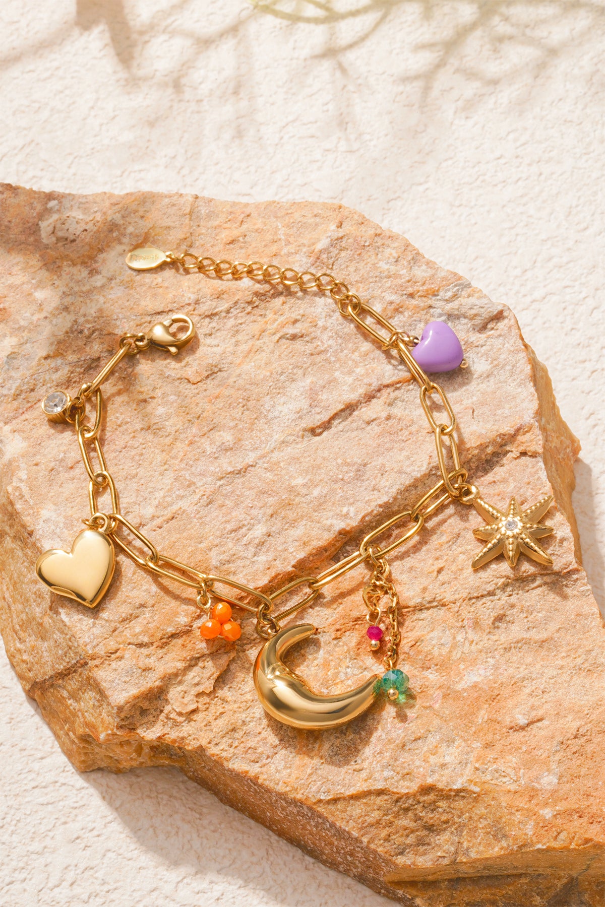 Charm bracelet artfully displayed on brown textured rock, showing detailed charms and vibrant colour contrasts