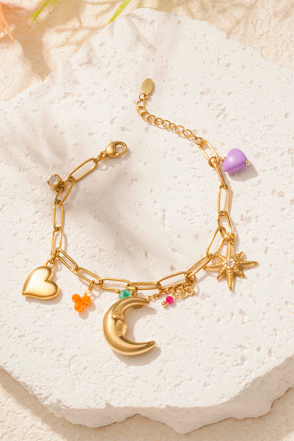 Moonlight charm bracelet on textured white stone with golden charms and colourful beads catching light