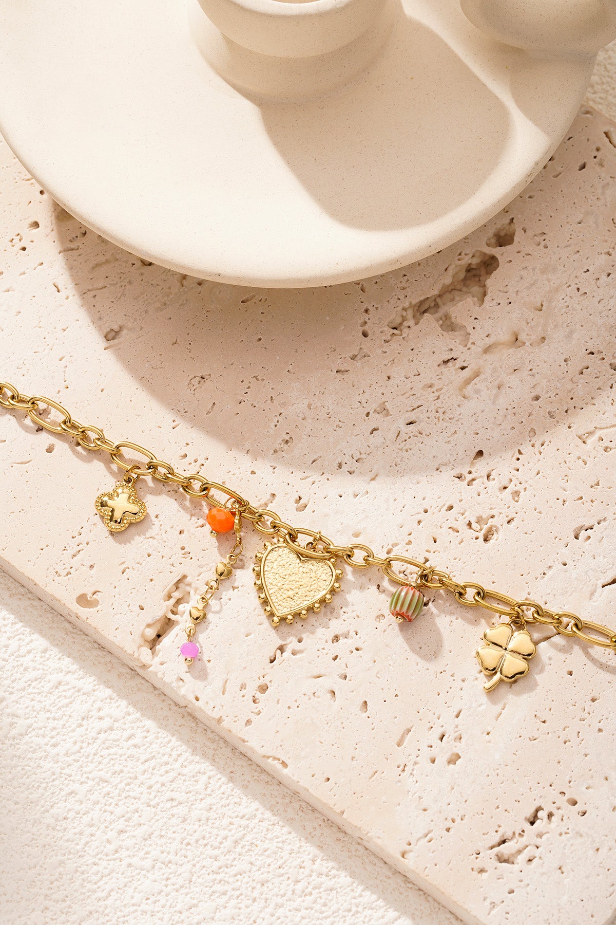 Gold charm bracelet artfully arranged on a textured beige surface with soft natural lighting