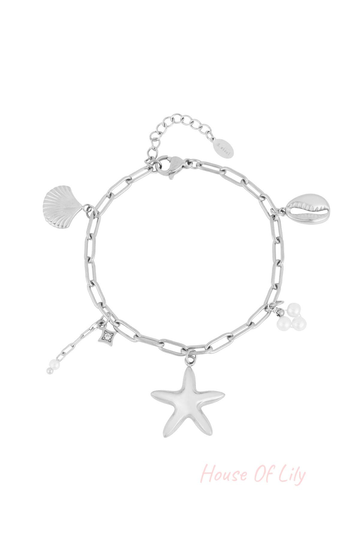 Silver-tone chain link charm bracelet with starfish, shell, cowrie shell and pearl charms laid flat on white background