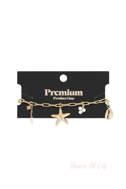 Gold-tone seaside charm bracelet displayed on black card labelled Premium Product Line