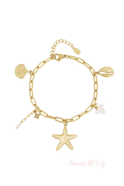Gold-tone chain link charm bracelet featuring starfish, seashell, cowrie shell and pearl cluster charms laid flat on white background