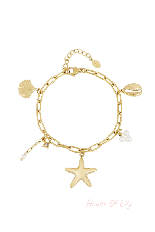 Gold-tone chain link charm bracelet featuring starfish, seashell, cowrie shell and pearl cluster charms laid flat on white background