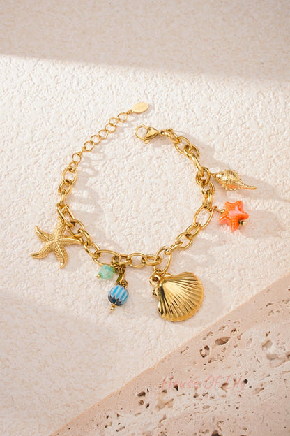Close-up of gold charm bracelet on textured white table surface highlighting detailed textures of shell and starfish charms