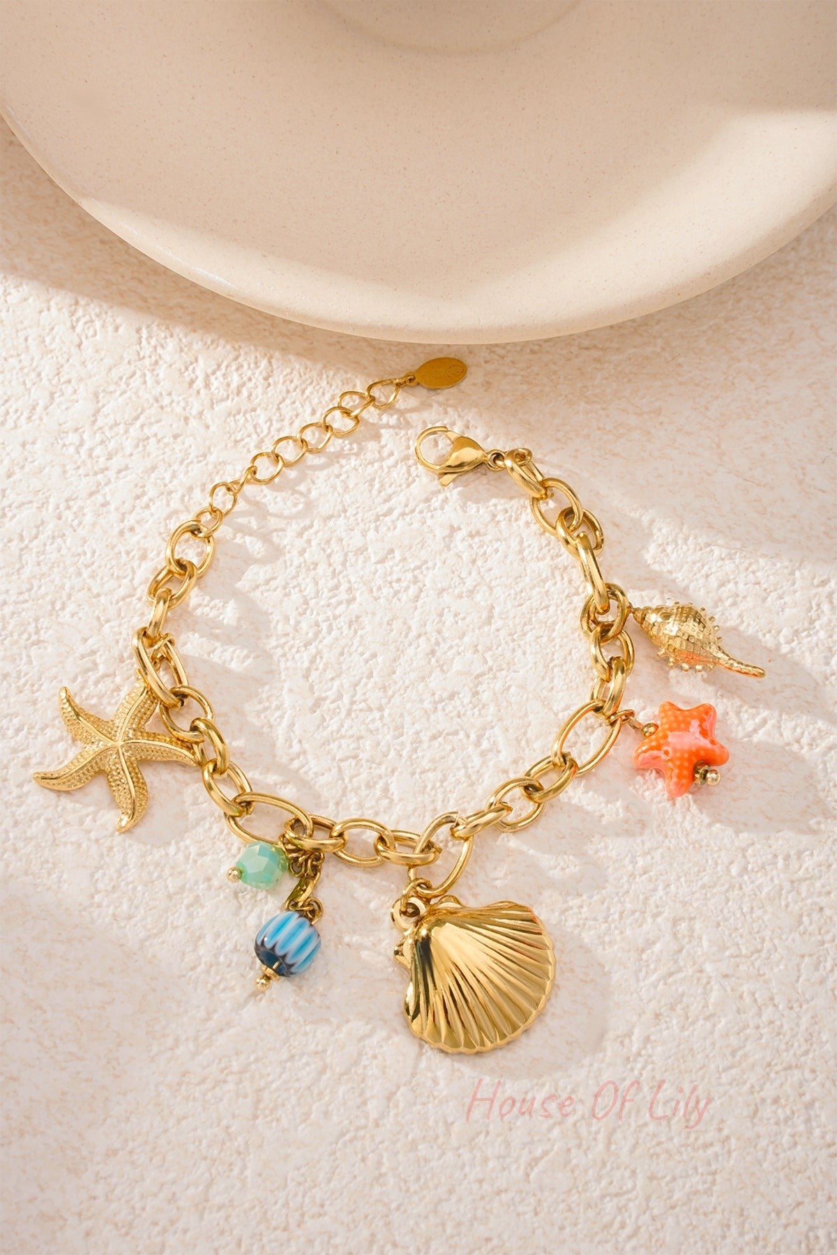 Gold charm bracelet laid flat on textured white surface with natural sunlight, showcasing all ocean-themed charms clearly