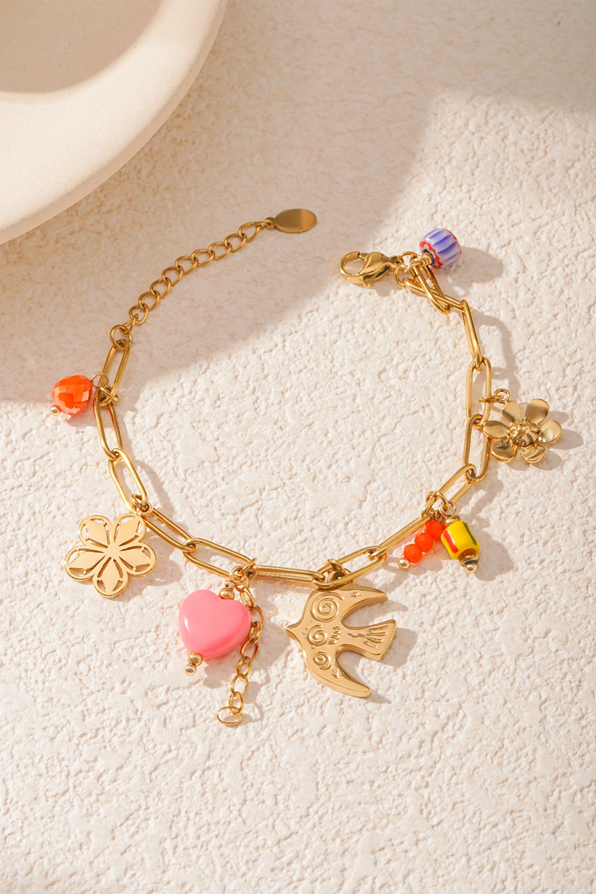Stylish golden charm bracelet arranged near ceramic plate on light surface emphasizing boutique aesthetic