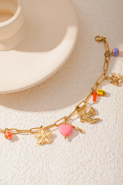 Detailed view of golden bracelet charms including pink heart, bird, and colorful beads shining in natural light