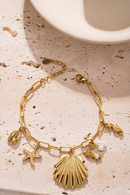Golden shell charm bracelet placed on textured beige background showcasing lobster clasp and delicate charms