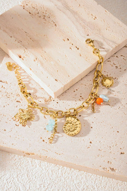 Detailed view of bracelet on textured cream stone showing gold links and ocean-themed charms with bead accents