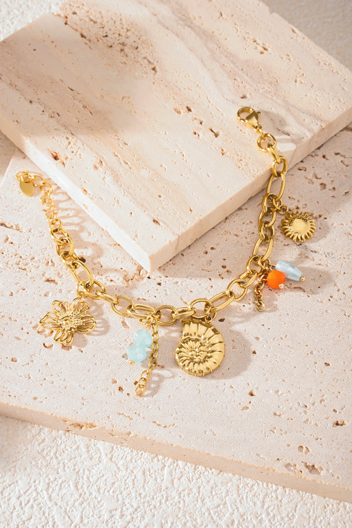 Detailed view of bracelet on textured cream stone showing gold links and ocean-themed charms with bead accents