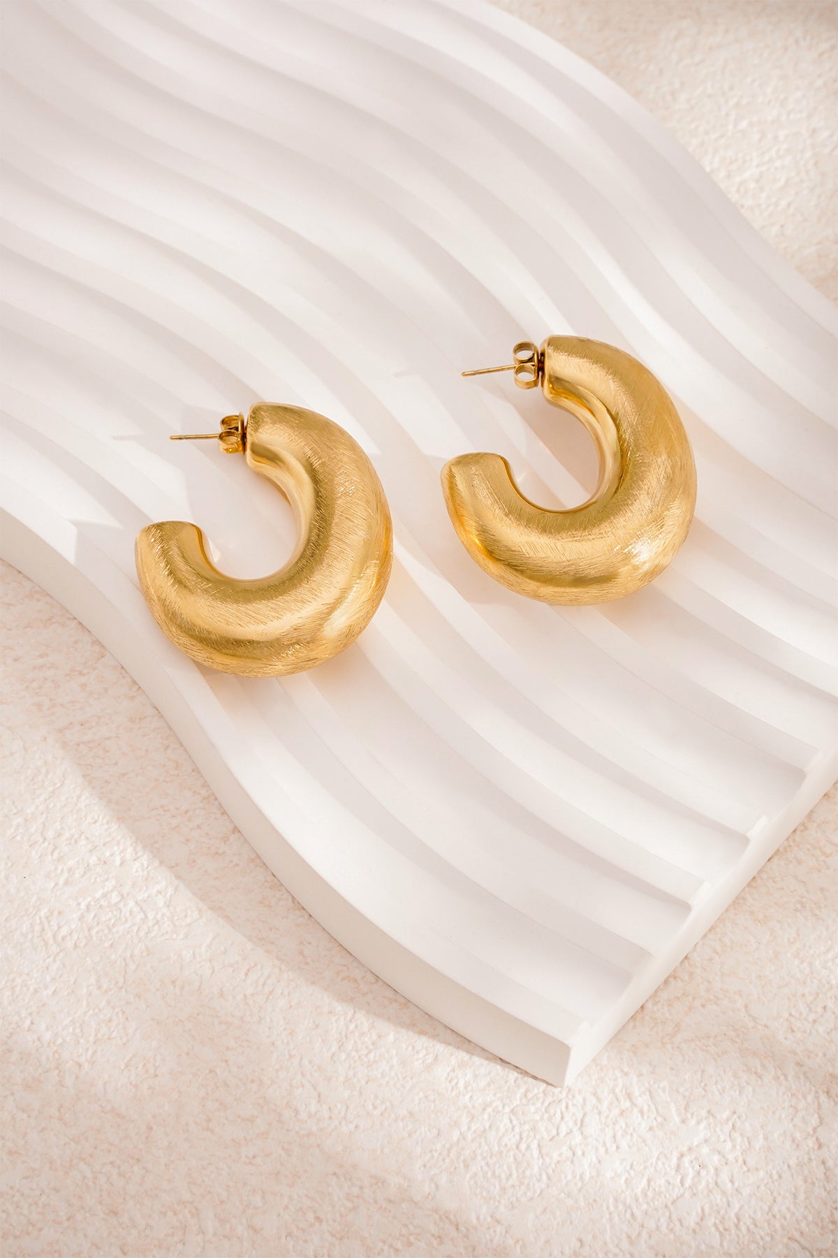 Chunky brushed silver hoop earrings posed in front of natural stone background