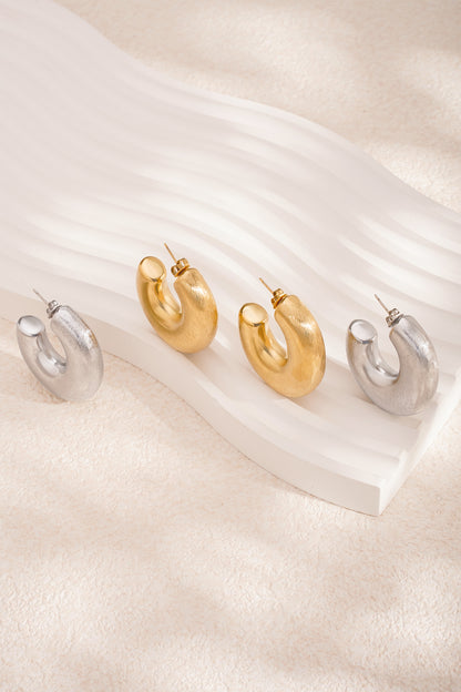 Close-up of two pairs of chunky hoop earrings, gold and silver, on sculptural white display