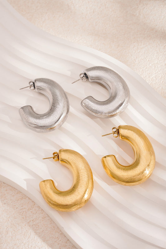 Four chunky hoop earrings in brushed gold and silver on wavy white textured tray