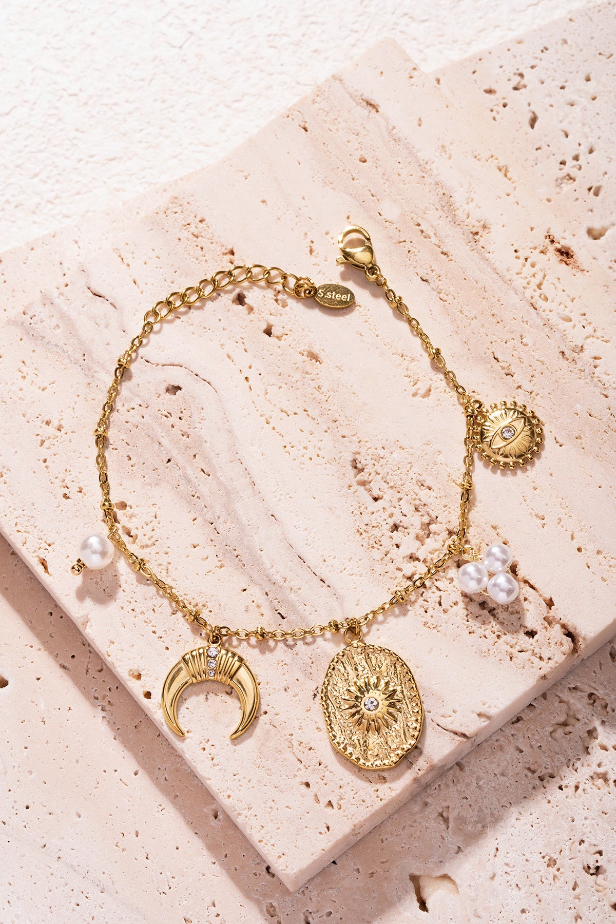 Gold-tone bracelet with charms shown atop textured beige stone slab