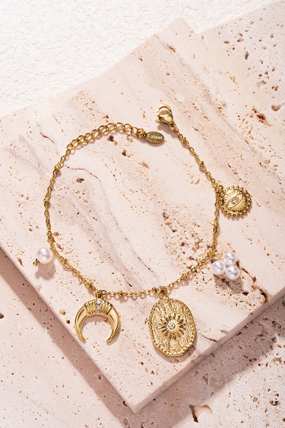 Gold-tone bracelet with charms shown atop textured beige stone slab