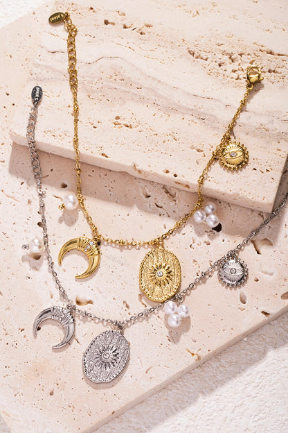 Multiple charm bracelets with gold and silver crescent moons, textured sun medallions, and pearl clusters on stone slabs