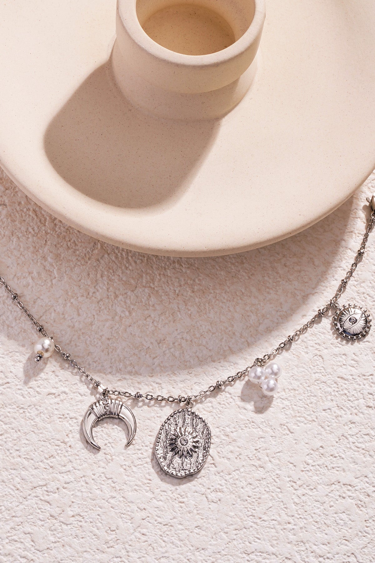 Silver-tone charm bracelet with crescent moon, sun medallions, and pearl charms on textured stone background