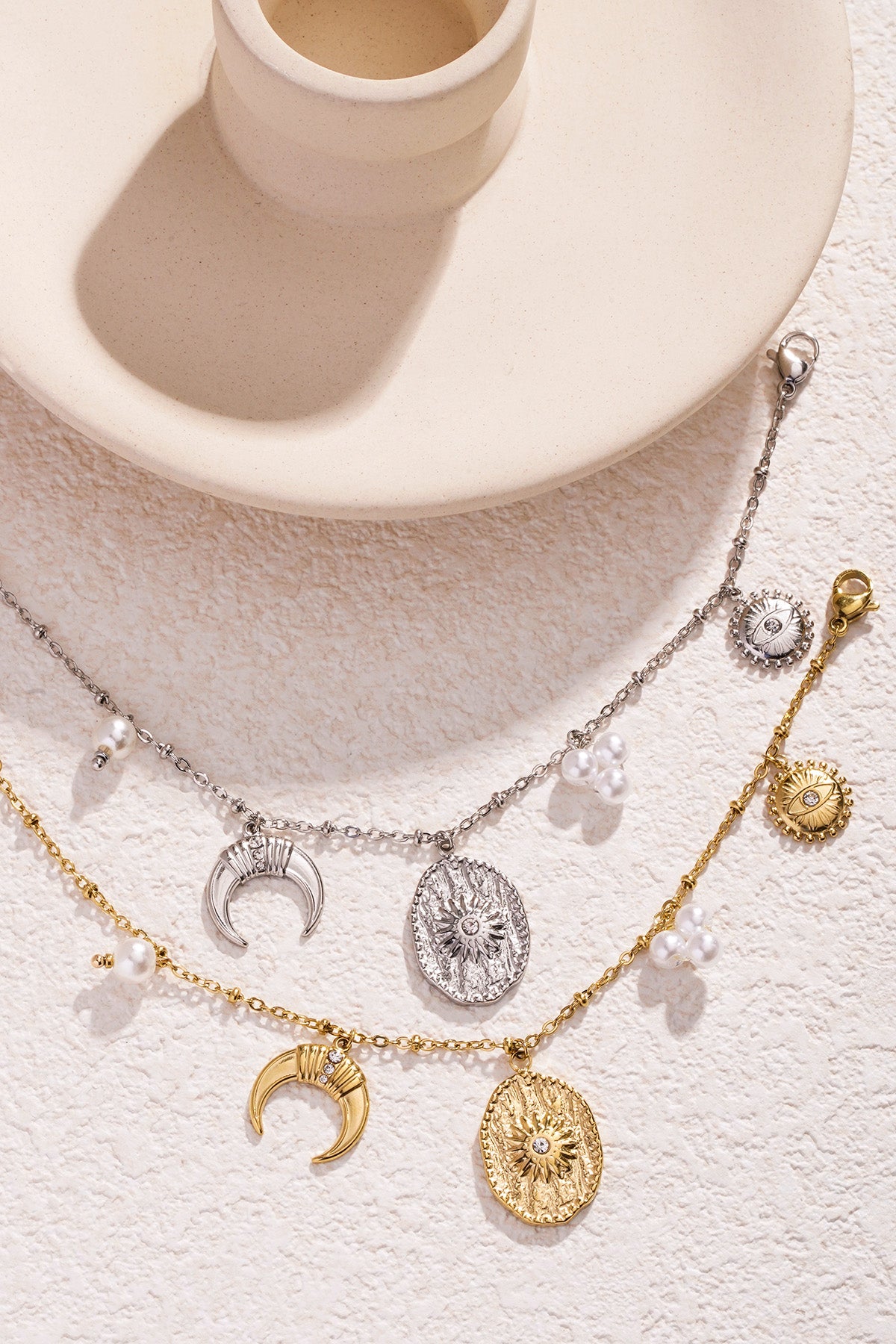 Gold and silver charm bracelets arranged on light stone backdrop near decorative ceramic piece