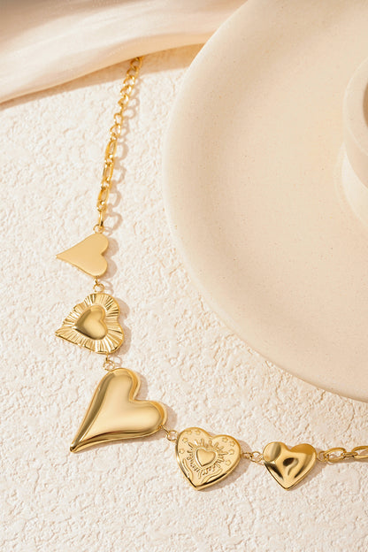 Gold chunky heart charm bracelet close-up on a cream textured surface beside a circular white decorative object